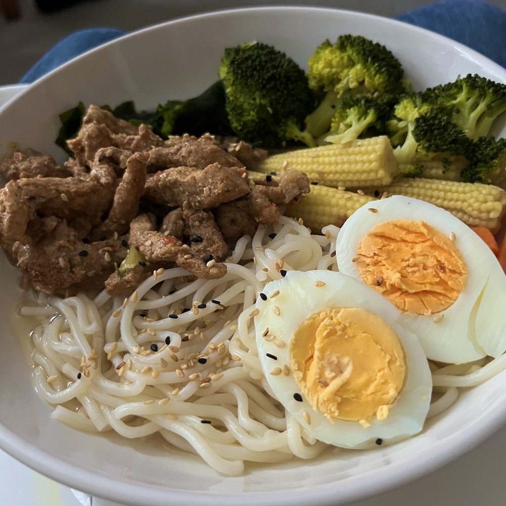 Noodles, egg, baby corn, and steak with a broth in a white bowl